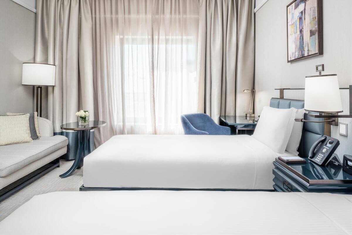Een hotelkamer met een bed, een bureau, een stoel, een lamp en een schilderij aan de muur.