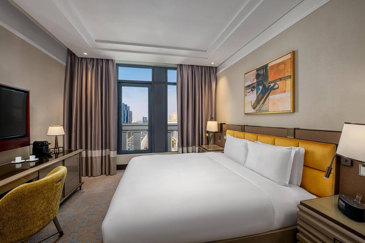 Een hotelkamer met een groot bed, een bureau met een televisie, een stoel en een raam met gordijnen.