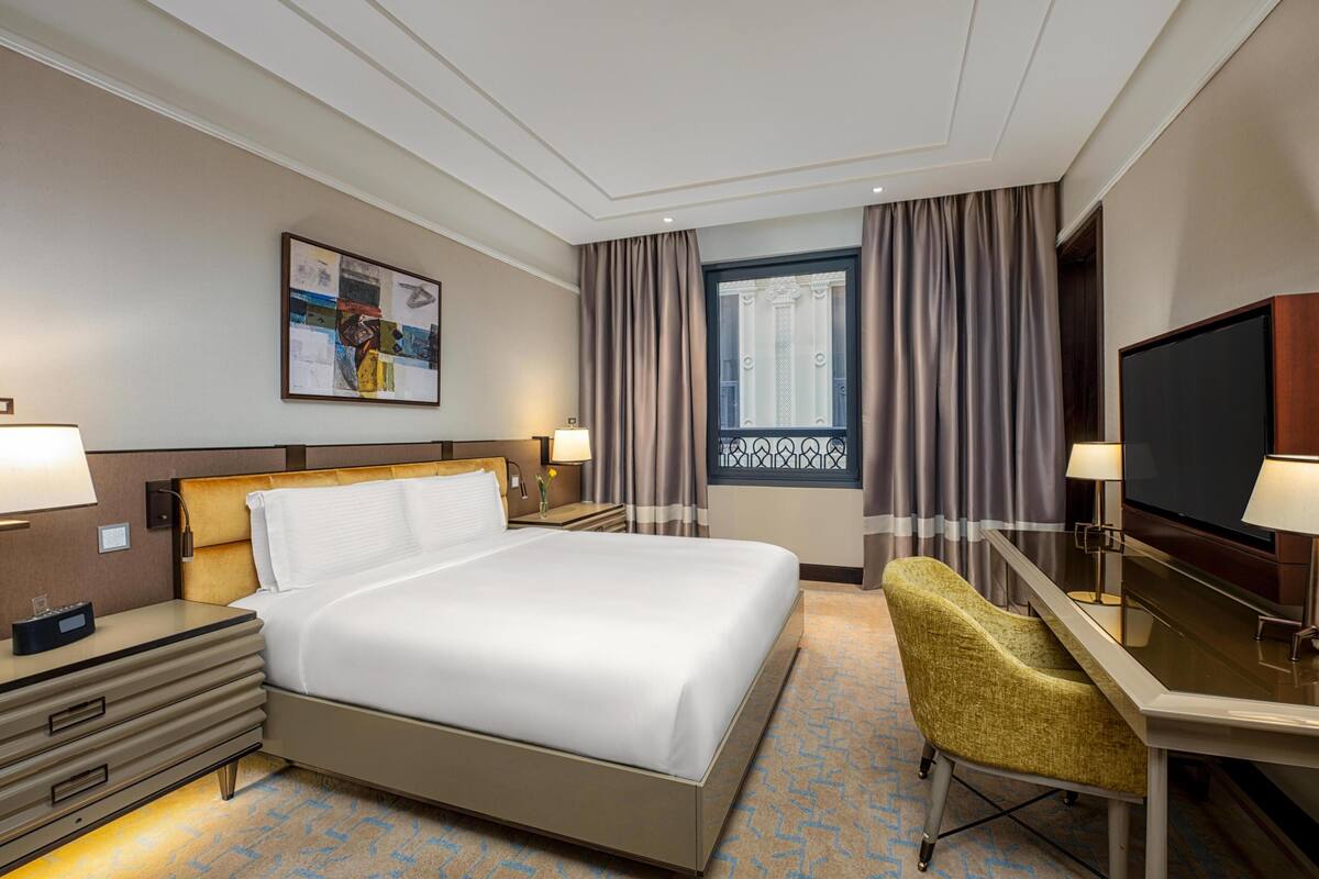 Een hotelkamer met een bed, een bureau, een televisietoestel en een raam met gordijnen.