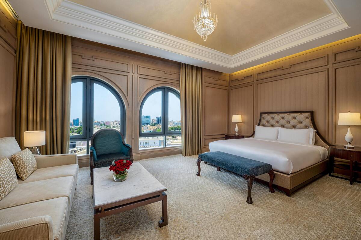 Een hotelkamer met een groot bed, een slaapbank, een tafel met een bloevas, twee lampen en een kroonluchter.