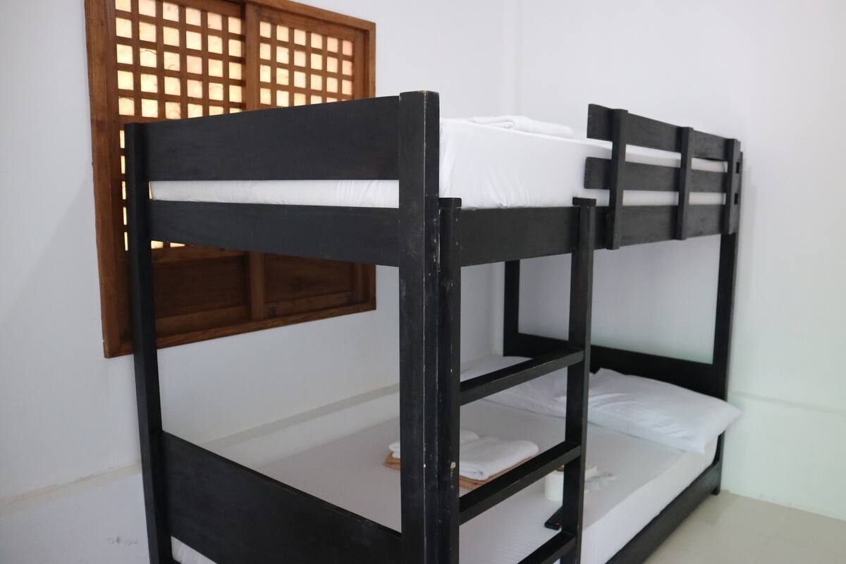 A bunk bed with white bedding, a wooden headboard, and a window with a wooden lattice.