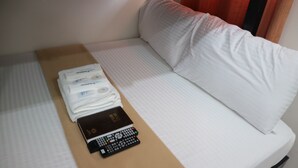 A neatly made bed with white sheets, a folded white towel, and a remote control on a beige surface. - La Patricia de Baler (Baler)