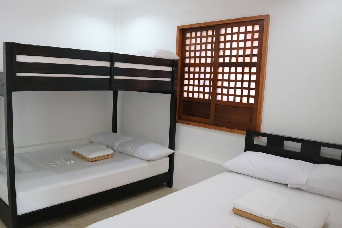 A bunk bed with a wooden frame and white bedding. There is a window with a wooden lattice design.