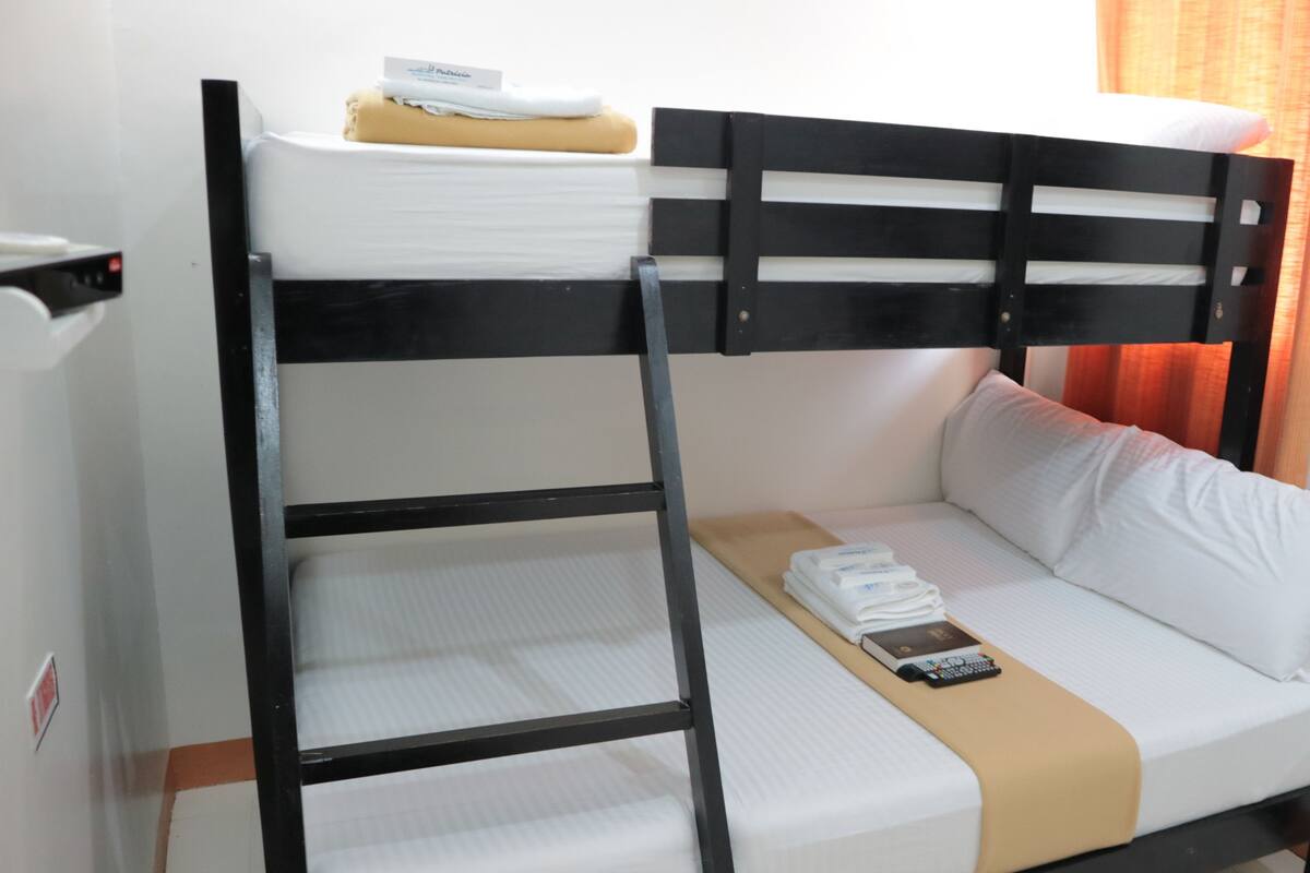 A bunk bed with a white mattress and a beige blanket. There is a remote control on the lower bunk.