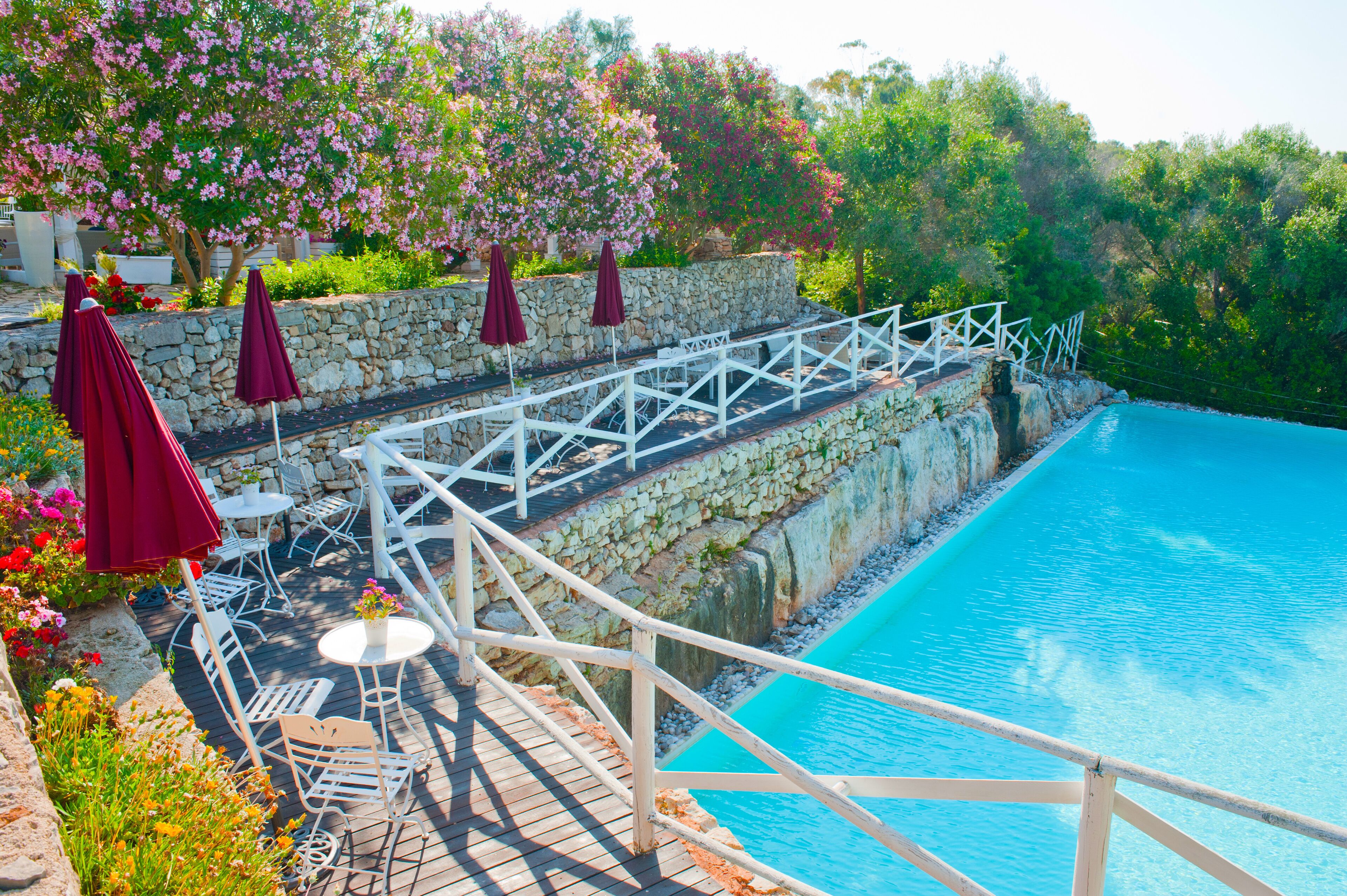 Un espace aménagé au bord de la piscine, avec des murs en pierre, des garde-corps blancs et des sièges d’extérieur.