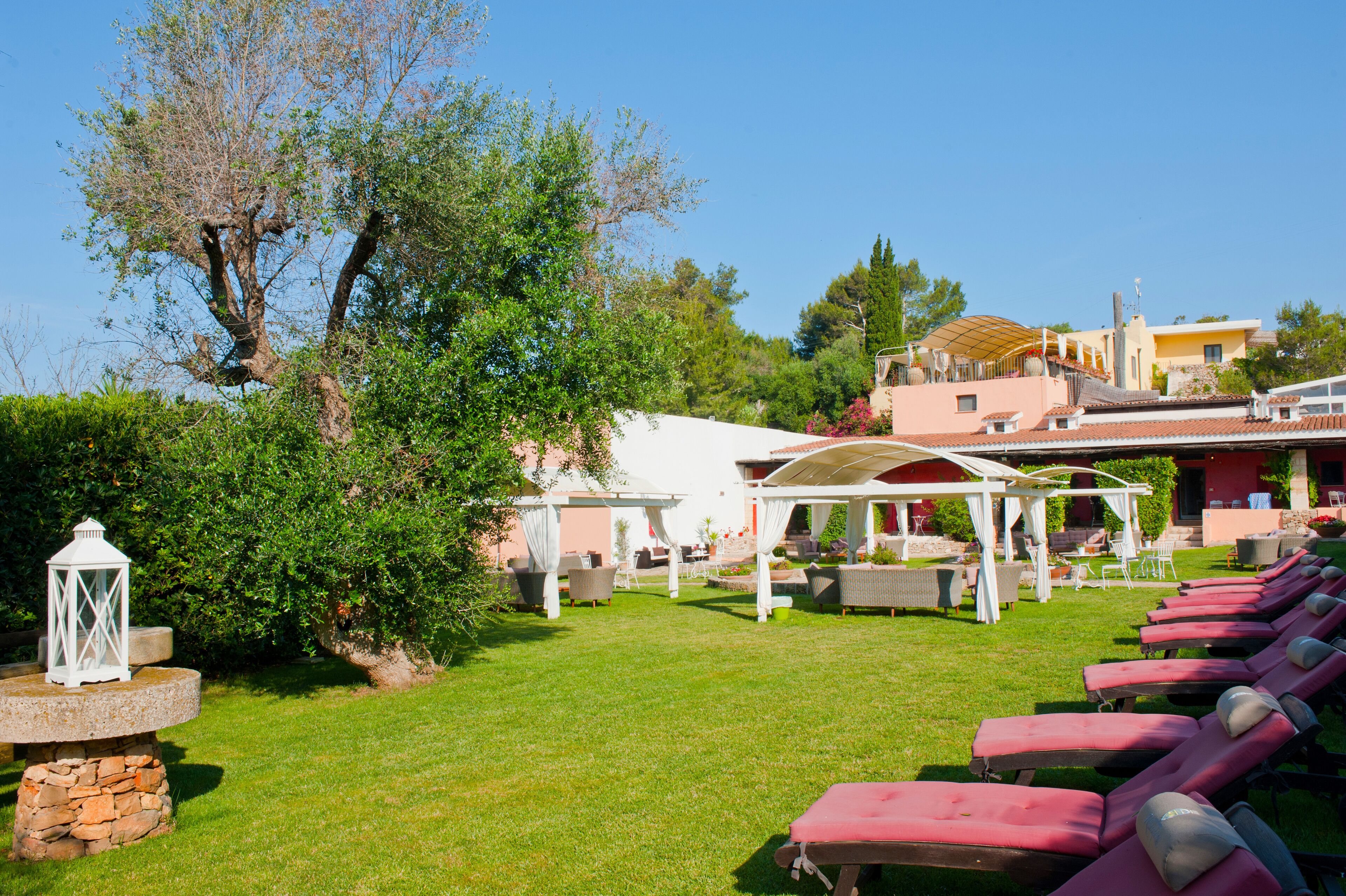 Ein Garten mit einer Pergola, Liegestühlen und einem Steintisch mit einer Laterne.