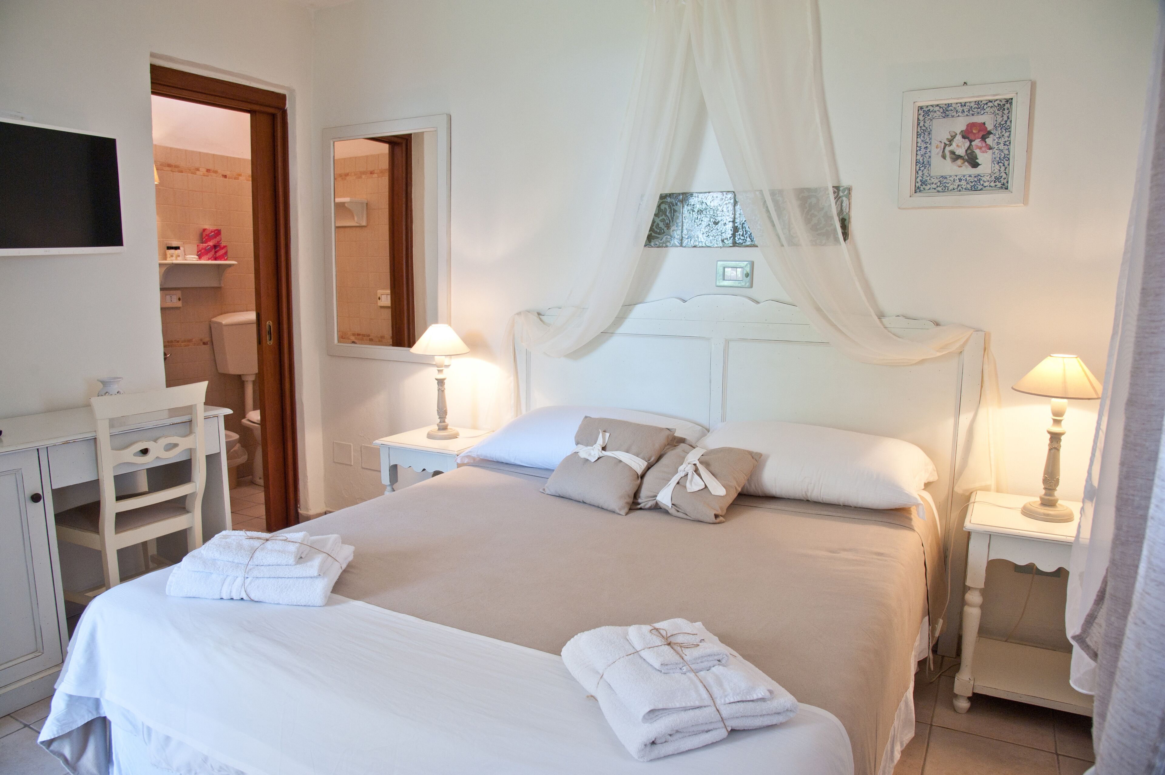 A neatly arranged bedroom with a large bed, two bedside tables with lamps, a wardrobe, and a mirror.