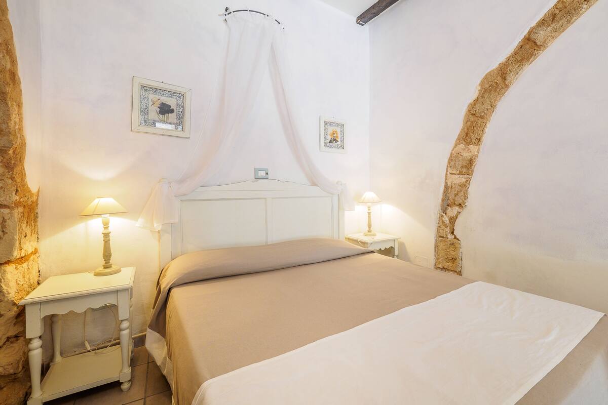 Ein Schlafzimmer mit einem Bett, zwei Nachttischen mit Lampen, einem weißen Kopfteil und zwei gerahmten Bildern an der Wand.