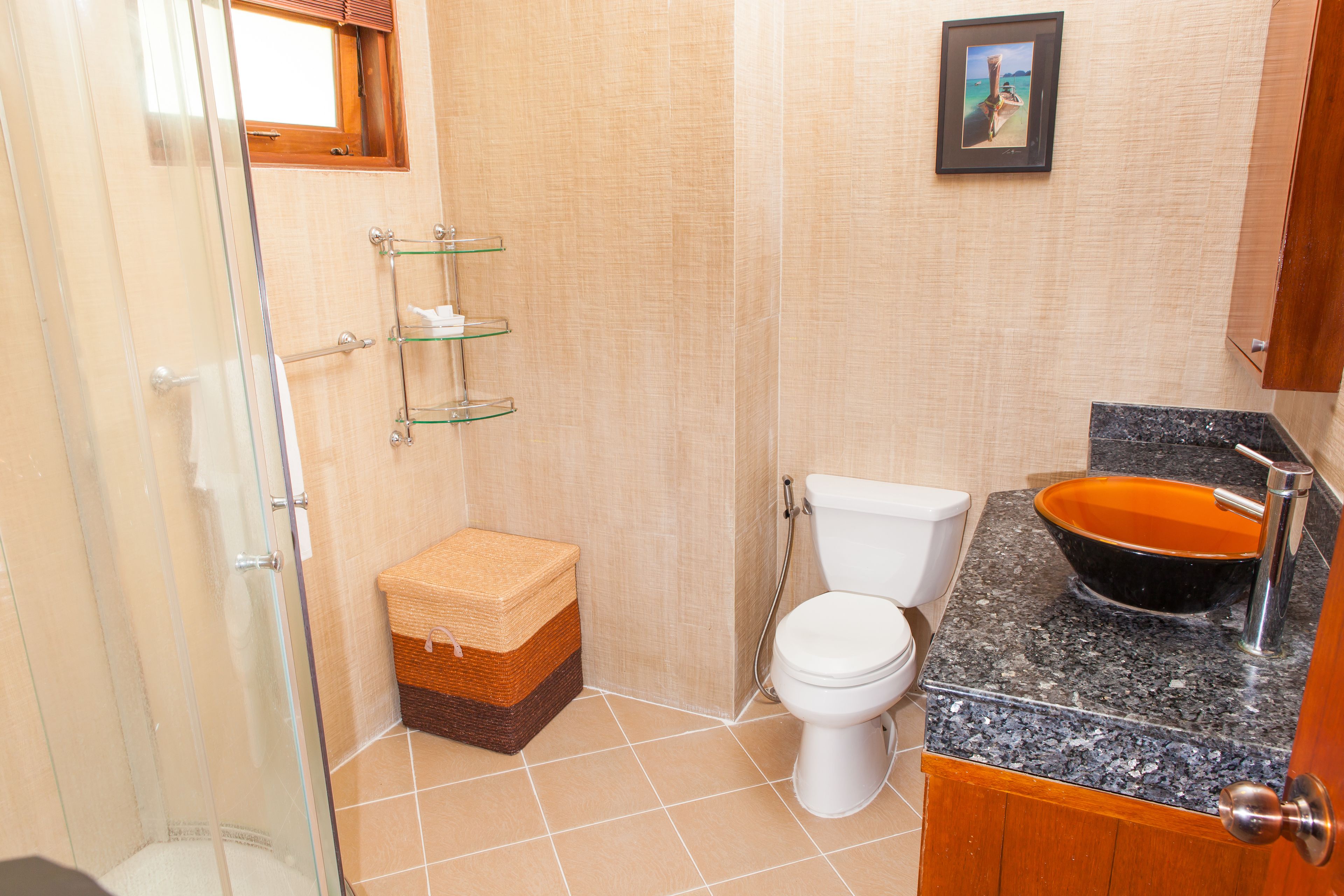 A bathroom with a glass shower enclosure, a toilet, a sink with a bowl, and a framed picture on the wall.