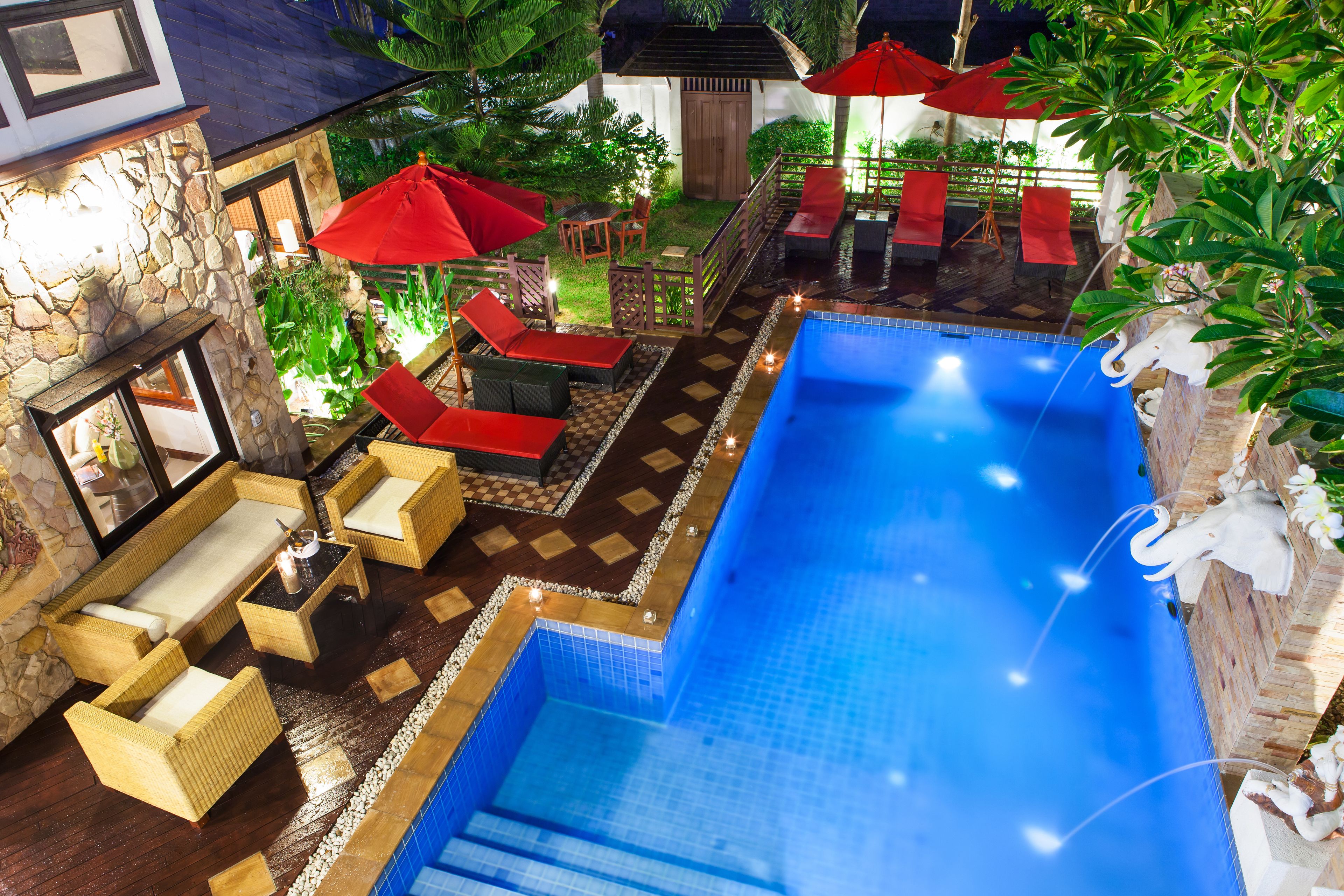 A rooftop pool area with lounge chairs, umbrellas, and a stone wall.