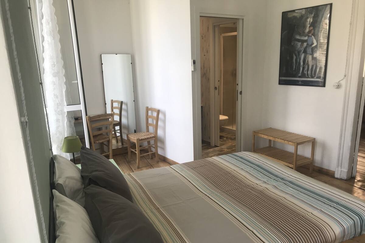 A bedroom with a bed, a chair, a small table, and a door leading to a bathroom.