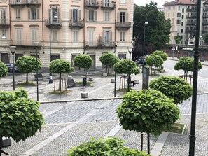 A cobblestone square with evenly spaced trees and benches, surrounded by historic buildings with balconies. - La Casa di Arturo (Turin)