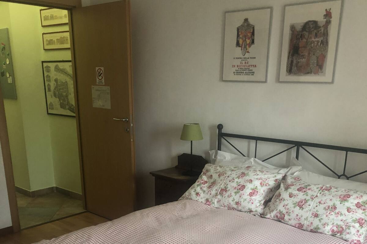 A bedroom with a bed, a nightstand, a lamp, and two framed posters on the wall.
