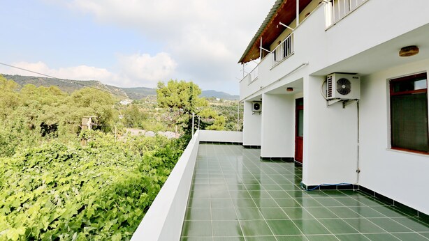 Un edificio con terraza de tejas verdes, paredes blancas y unidades de aire acondicionado.