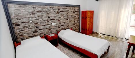 Habitación de hotel con dos camas individuales, cabecero de madera, armario rojo y una ventana grande con cortinas.