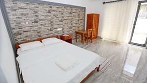 Una cama bien hecha con sábanas blancas, un cabecero de madera, una mesita de madera con una silla y una pared con diseño de piedra.