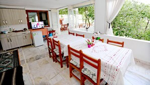 Un comedor con mesa y sillas, una cocina al fondo y vistas a la vegetación por la ventana.