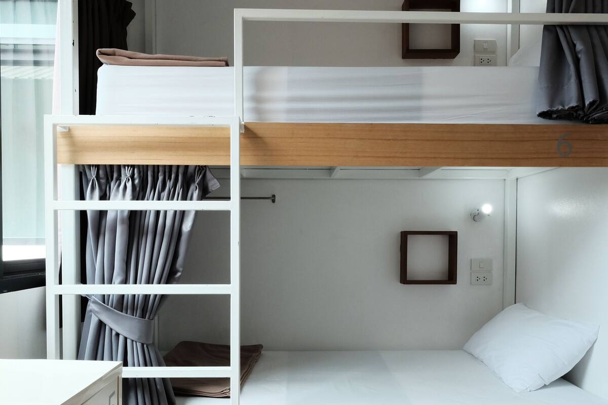 Ein Schlafraum mit Etagenbetten, Holzboden, Schreibtisch mit Schubladen und einem Vorhangfenster.
