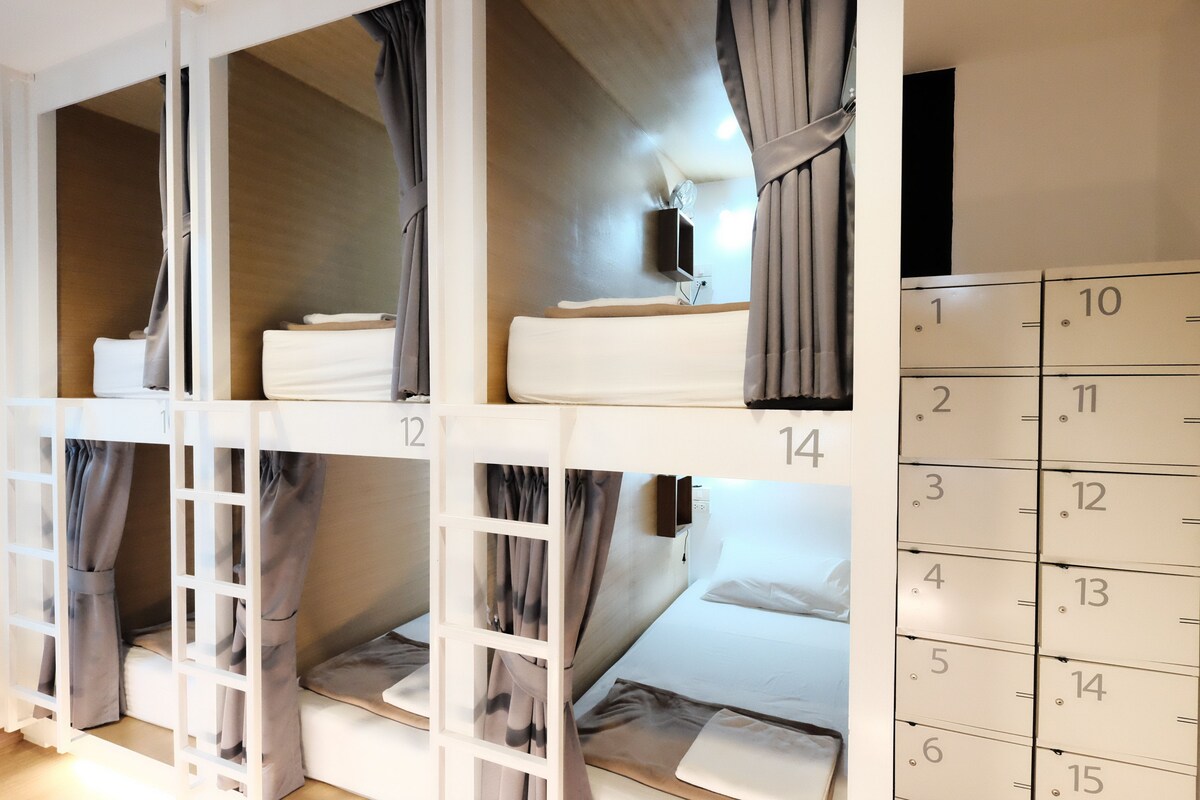 Une chambre d’hôtel avec des lits superposés, un calendrier et une petite table avec une lampe.
