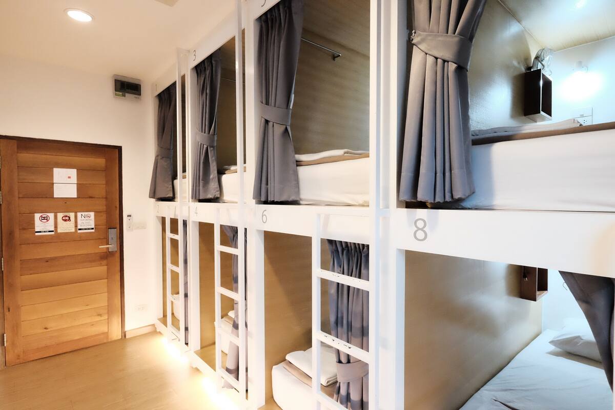 Ein Schlafsaalzimmer mit Etagenbetten, nummeriert von 3 bis 8, Holztüren und einem kleinen Fernseher an der Wand.