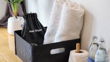 A black hair dryer bag, two white towels, a roll of toilet paper, and two bottles of water on a wooden table.