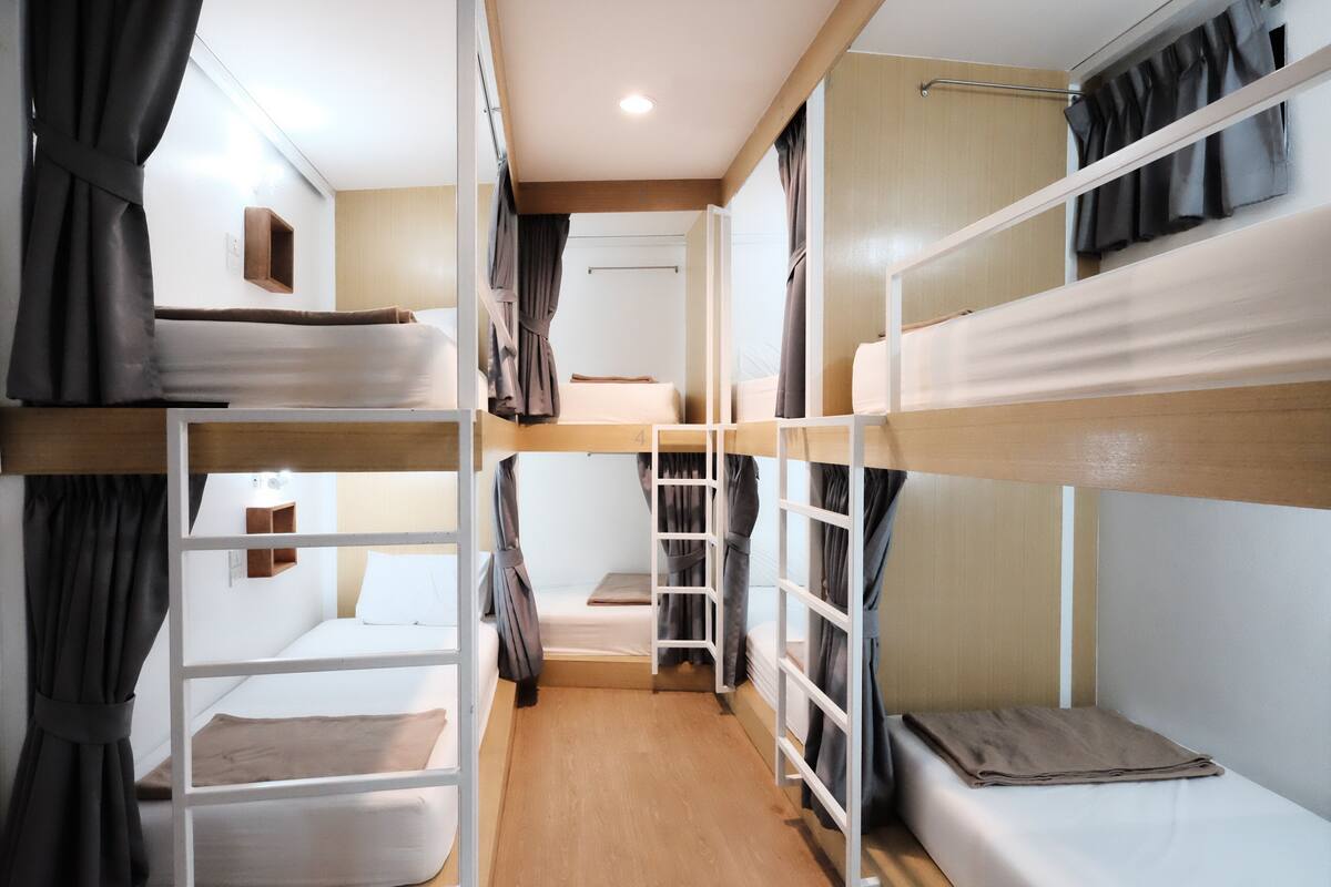 Ein Schlafsaal mit Etagenbetten, Holzboden, weißen Wänden und Vorhängen.