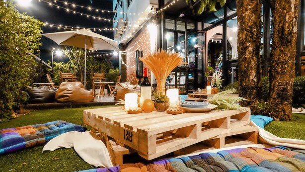 Un espace de restauration en plein air avec une table en bois, des bougies et divers coussins.