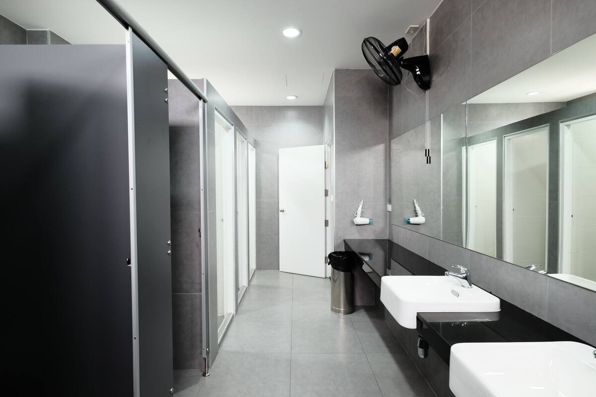 Ein modernes Badezimmer mit zwei Waschbecken, einem Spiegel, einem Ventilator und einem Mülleimer.
