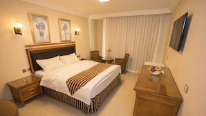 A hotel room with a large bed, a wooden nightstand, a desk with a bowl of fruit, and a television on the wall. - Dweik Hotel 3 (Aqaba)