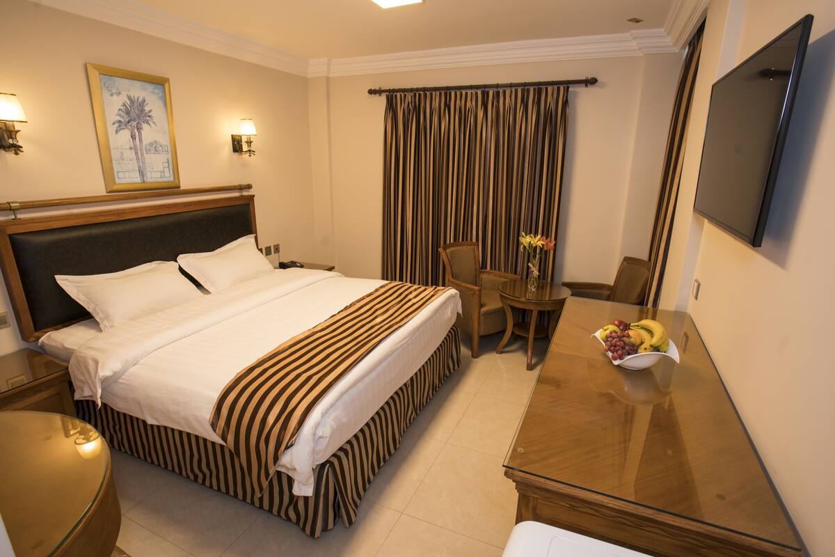 A hotel room with a bed, a desk, a chair, a TV, and a window with curtains.