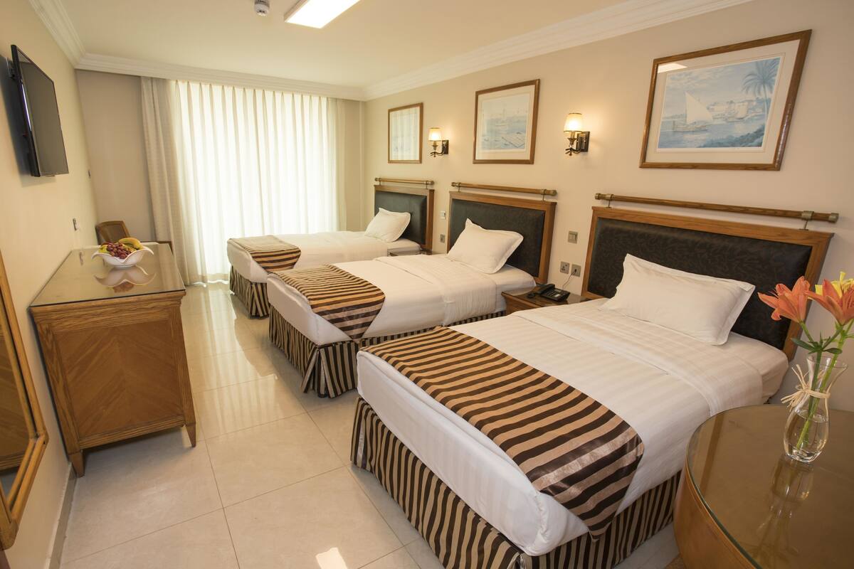 A hotel room with two beds, a desk, a TV, and framed artwork on the walls.