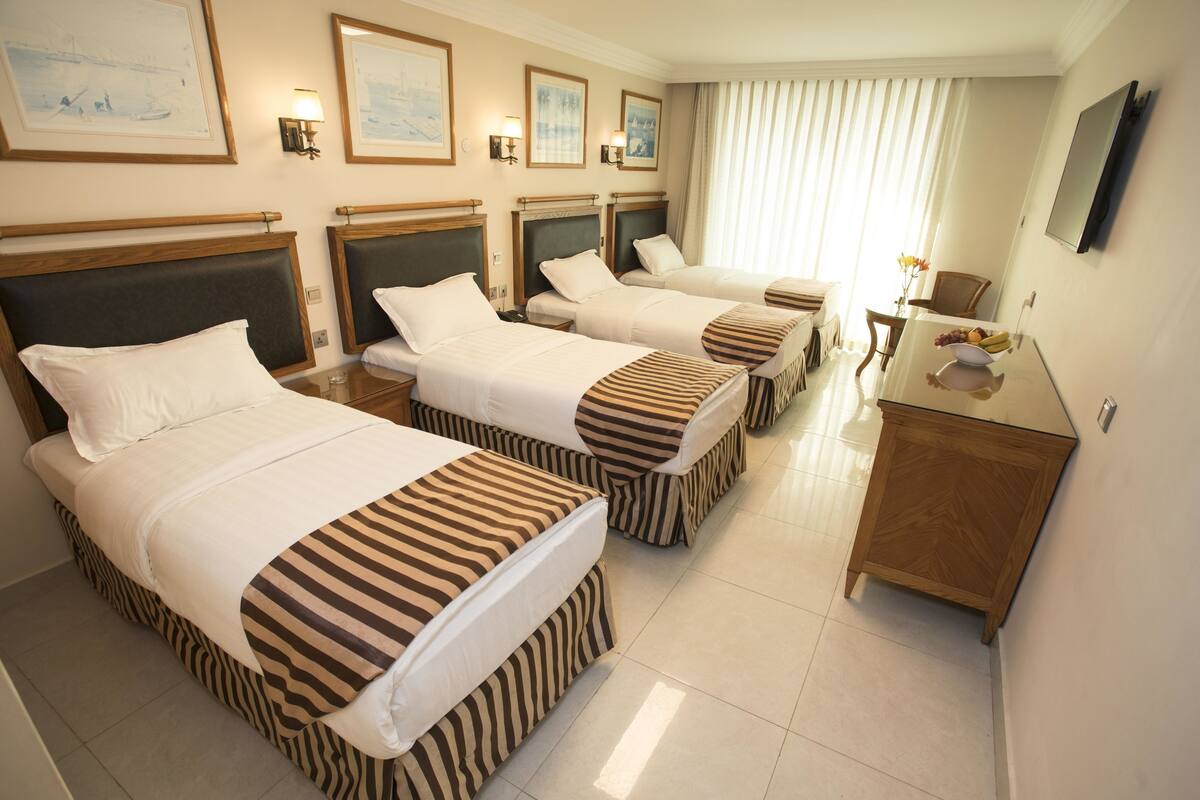 A hotel room with three beds, a wooden cabinet, and a dining table with a vase of flowers.