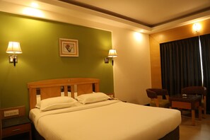 A hotel room with a large bed, two bedside lamps, a small table with chairs, and a picture on the wall. - Dr. Rajkumar International Hotel (Bengaluru)