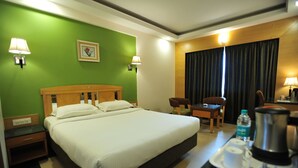 A hotel room with a large bed, a desk with a chair, a coffee maker, and a water bottle on the tray. - Dr. Rajkumar International Hotel (Bengaluru)