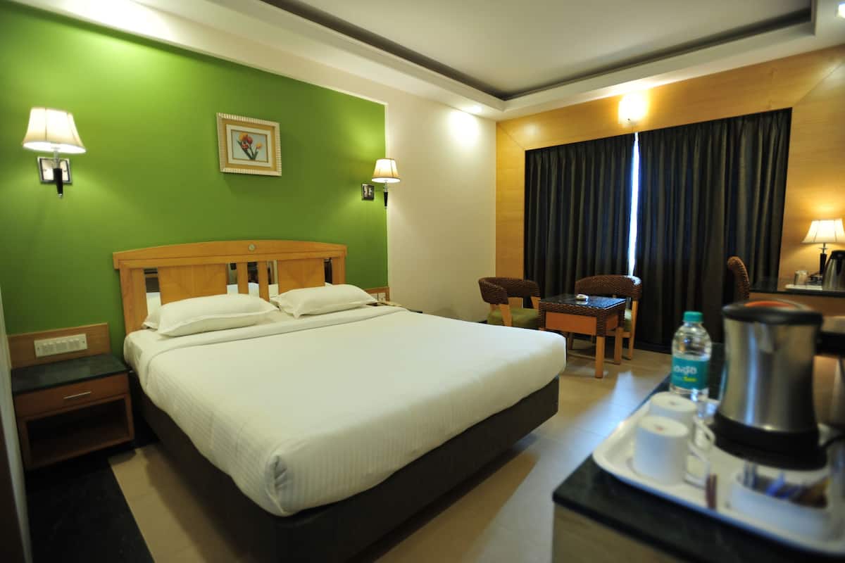 A hotel room with a large bed, a desk with a chair, a coffee maker, and a water bottle on the tray.