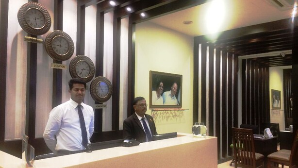 A reception area with a counter, clocks, and a framed photo on the wall. - Dr. Rajkumar International Hotel (Bengaluru)