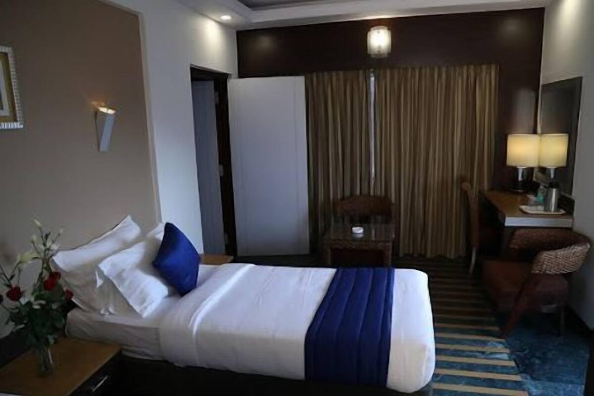 A hotel room with a bed, a desk, a chair, a lamp, and a curtain.