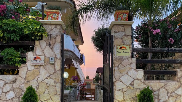 Une porte d’entrée en pierre, surmontée d’une enseigne indiquant « Casa Scirocco » et d’une adresse de site web.