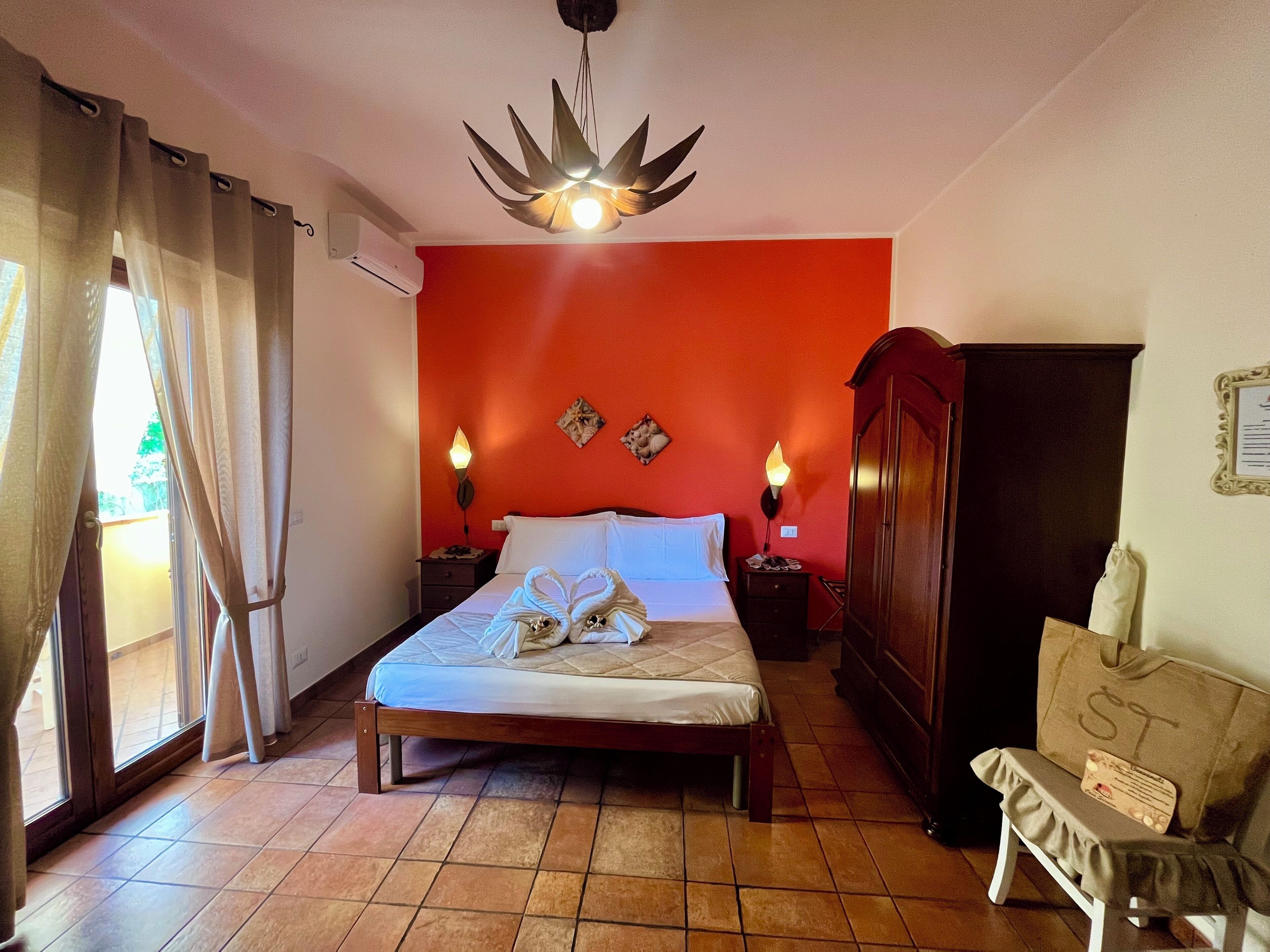 A bedroom with a bed, two bedside lamps, a wooden wardrobe, a bench, and a window with curtains.