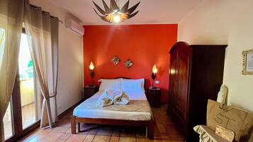 A bedroom with a bed, two bedside lamps, a wooden wardrobe, a bench, and a window with curtains.