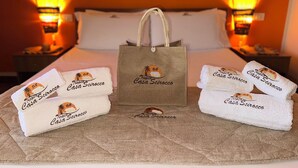 Une chambre d’hôtel avec un lit, deux tables de chevet, une lampe et un sac marron arborant le logo « Casa Scrocco ».