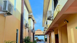 A narrow corridor with air conditioning units, potted plants, and a view of a building with a tiled roof. - Anyavee Nam Mao Beach Resort (Krabi)