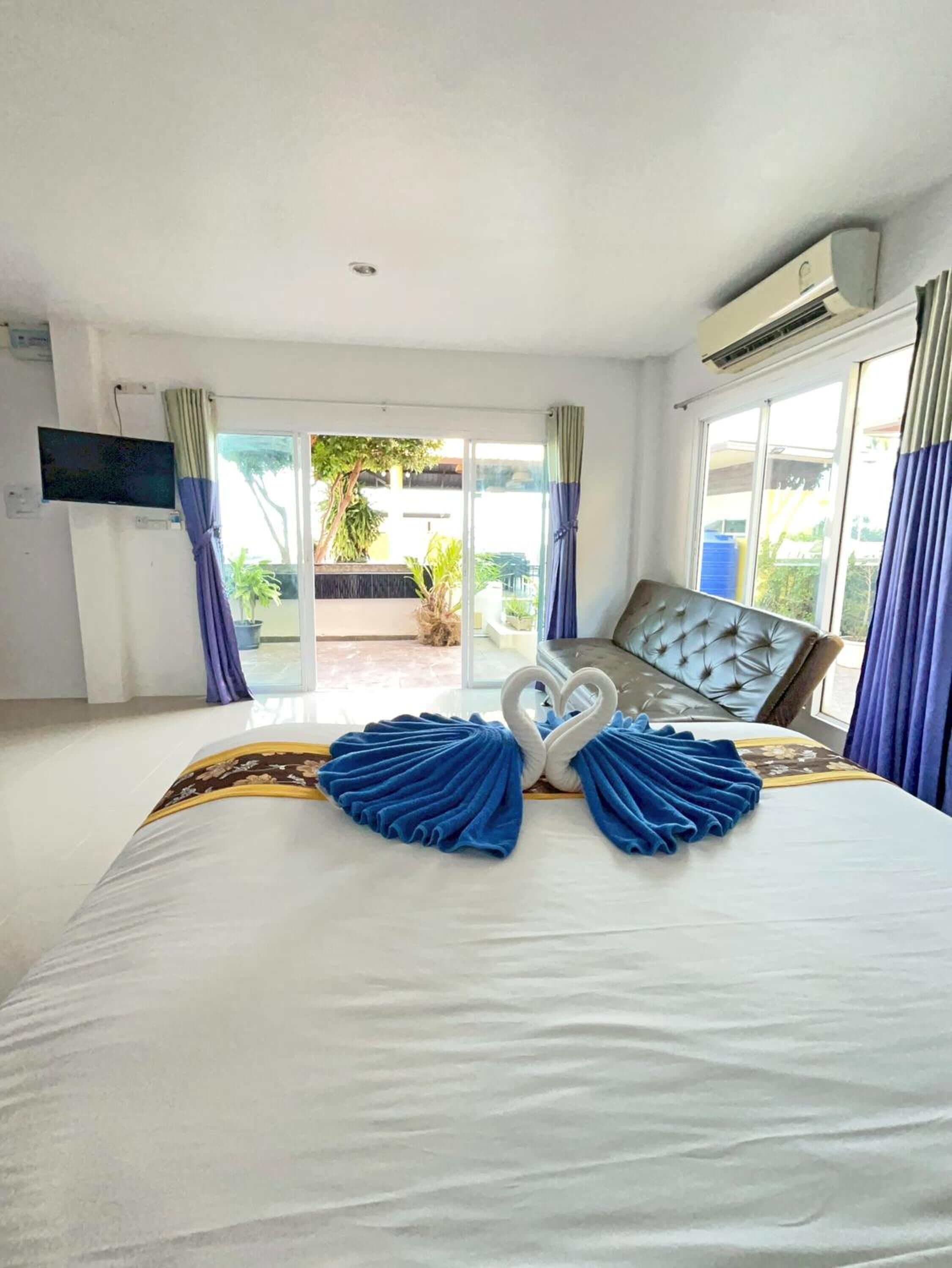 Habitación de hotel con cama, televisor de pantalla plana y puerta corredera de vidrio que da a un espacio exterior con plantas.