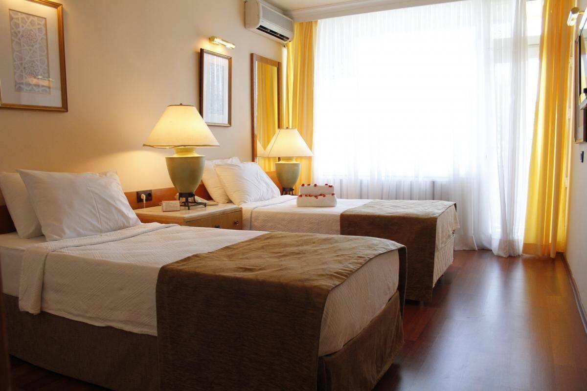 A hotel room with two beds, each with a lamp and a bedside table.