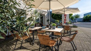 An outdoor seating area with wicker chairs and tables, a large umbrella, and a sign that reads "HOTEL". - Hotel Bergheim an der Erft (Bergheim)