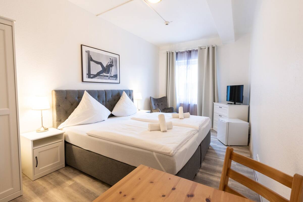 A hotel room with a bed, a desk, a chair, a TV, and a picture on the wall.