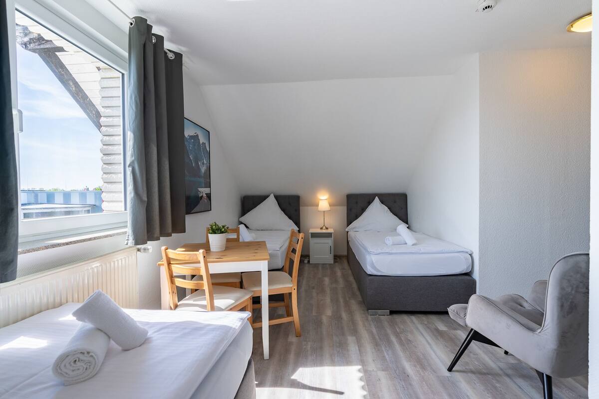 A compact hotel room with a bed, a small desk, a chair, a sofa, and a window with curtains.