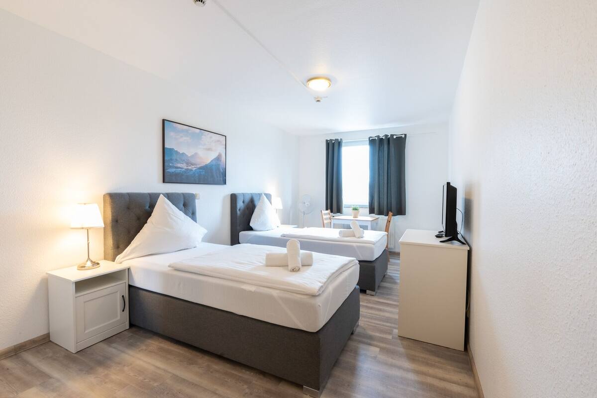 A hotel room with a large bed, a smaller bed, a desk, and a TV.