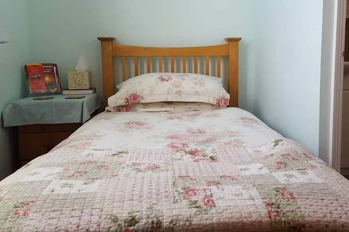 A bedroom with a wooden bed frame, floral bedding, a bedside table with a book and a tissue box.