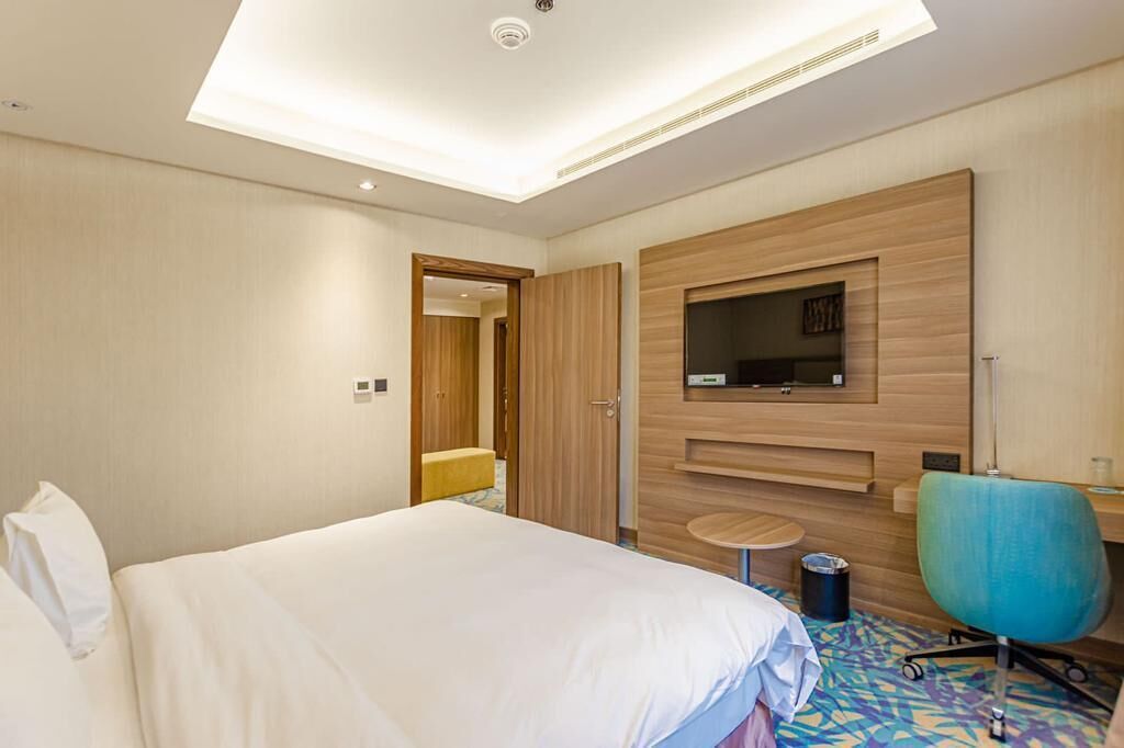 Ein Hotelzimmer mit Bett, Wandfernseher, Schreibtisch und Stuhl.